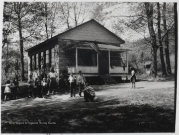 A group of school children play outside of the schoolhouse. Perhaps it is recess. Subjects unidentified. 