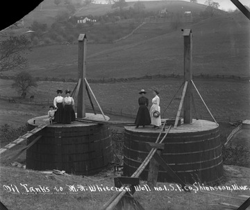 Unidentified women and one child stand on two oil tanks in an oil field in Shinnston, W. Va.