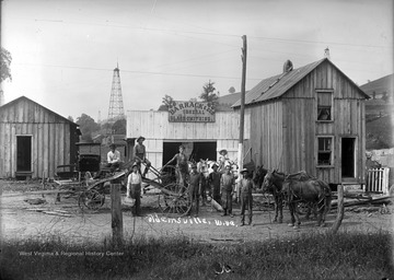 Group of unidentified men, a child, four horses, and a dog pose for a group portrait in front of Barrack & Son General Black-Smithing Store near Shinnston, W. Va.