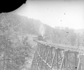 View of train on M and K Railroad carrying workers and lumber across a bridge.