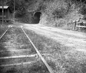 View of a tunnel, train tracks, dirt road, and portion of a small building.