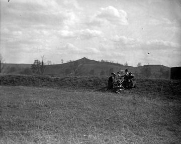A group of unidentified subjects are pictured on a hill with Dorsey's Knob in the background. 