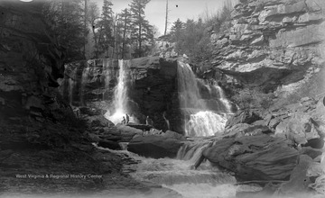 Four people climb across the rocks with a waterfall streaming from the cliffs in the background. Subjects unidentified. 