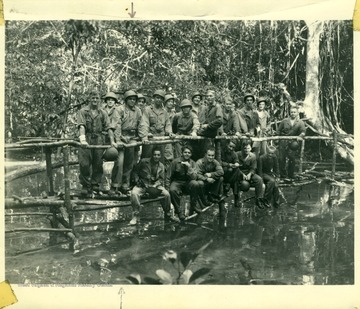 Marshall L. Williamson, U.S. Navy Medical Corps, second from the left in the front row of standing men, and the 57th Naval Construction Battalion (Seabees) standing on a bridge on the island of Espiritu Santo, within the New Hebrides.Written on the back of the photograph is this message: "Honey: Can you find me in this picture? If you can't just put the edge of a piece of paper on the two arrows and you can find me. P.S. I am second from the left in the first row of men who are standing."