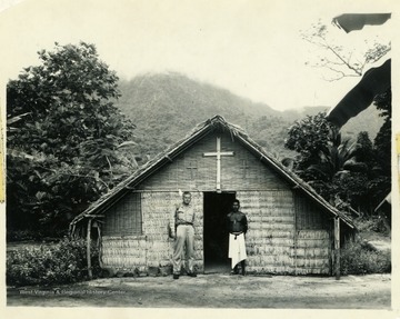 Marshall L. Williamson, U.S. Navy Medical Corps, assigned to the 57th Naval Construction Battalion (Seabees), stands with an islander at a chapel near his camp on the island of Espiritu Santo, within the New Hebrides.