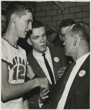 East Bank High School basketball coach Roy E. Williams, right, shakes the hand of Jerry West, left, in the dressing room after beating Mullens High School in Morgantown and winning the state championship title.West was East Bank's starting small forward. He was named All-State from 1953–56, then All-American in 1956 when he was West Virginia Player of the Year, becoming the state's first high-school player to score more than 900 points in a season.