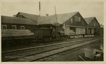 This image is part of the Thompson Family of Canaan Valley Collection. The Thompson family played a large role in the timber industry of Tucker County during the 1800s, and later prospered in the region as farmers, business owners, and prominent members of the Canaan Valley community.A man is seen standing in a train next to the Box Factory.