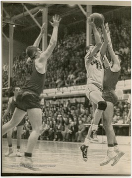West shoots a layup in front of a large auditorium of spectators.  West was named All-State from 1953 to 1956 in high school.  He led East Bank High School to the state championship in 1956.