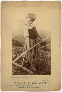 A small child holds a rake in a hay field in West Virginia while posing for this 'Rural Life in West Virginia' advertisement