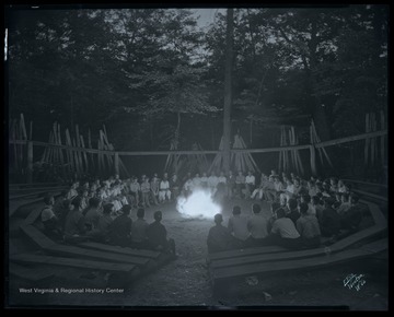 Campers gather around a fire in an unidentified location. 