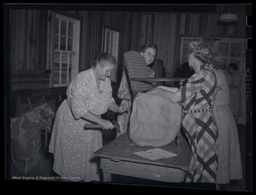 Four unidentified women assemble a chair together. The photo labels the location as the "R. E. Building."