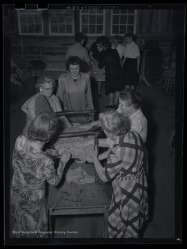 A group of unidentified women work together to assemble a chair. The photo describes this location as the "R. E. Building."