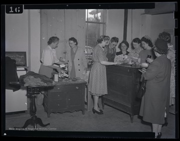 A group of women learn how to finish furniture properly. The photograph description identifies the location as the "R. E. Building."