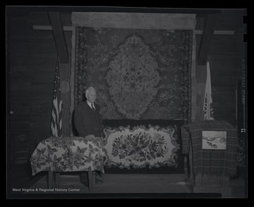A man stands beside the homemade rugs which are displayed prominently in an unidentified location