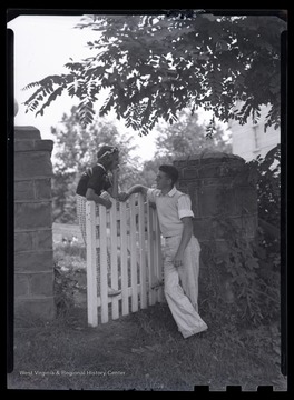 A female and male camper talk to each other as they hang around the wooden gate. 