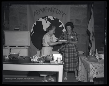 Two unidentified women handle food during a demonstration for young, female campers. 