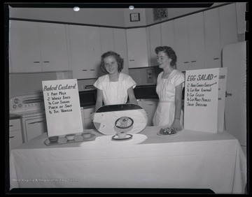Two unidentified women show female campers how to correctly bake custard. 