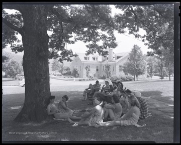 A group of older boys and girls relax under a tree's shade. Subjects unidentified. 