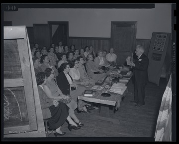 Eaton is pictured on the right, speaking to a large group of women.