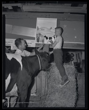 The young boy plays with the toy while balancing on a stack of hay.