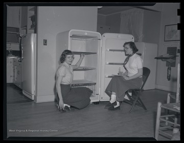 Two unidentified girls work with a refrigerator. 