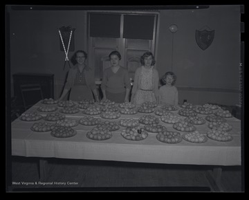 Four unidentified females pose beside the dozens of colored eggs produced at the 4-H meeting. 