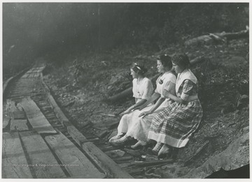 Three women sit by a wooden railroad track, used for logging and lumbering, in Wyoming County, W. Va.