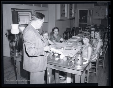 A man demonstrates how to properly change a light bulb to a group of women. Subjects unidentified. 