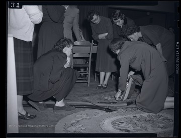 A group of women observe as another women demonstrates how to use a vacuum cleaner. Subjects unidentified. 