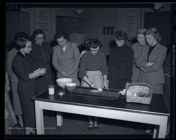Women observe as a woman demonstrates how to remove a stain from a cloth mat. Subjects unidentified. 