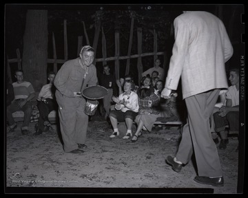 A boy holds a pail and a pan while people watch from the sidelines. Subjects unidentified. 