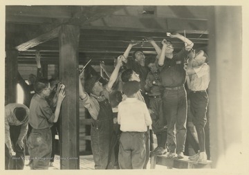 A group of young men and boys place electrical wiring along wooden beams. Subjects unidentified.  Subjects are likely members of a 4-H organization.