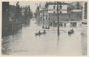 Photo postcard of an unidentified intersection in Wheeling, W. Va., likely Market Street or nearby. Several business signs are visible. Postcard is part of a souvenir book of 1913 flood images.