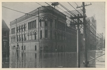 Photo postcard of a building located at the intersection of 16th Street and Main Street during a 1913 flood in Wheeling, W. Va. Postcard is part of a souvenir book of 1913 flood images.