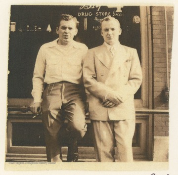 Two men sitting on a rail outside The Big 4 Drug Store, located on the corner of 3rd Avenue and Temple Street, in Hinton, W. Va.  A membership card identifies K. D. Foster, on the right, as the Vice President of The Rail Club.