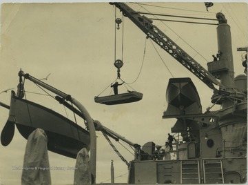 A sailor stands in the boat while it's being raised by the battleship's crane. The "punt" boat was used only to paint the sides of the ship. The boat pictured on the far left is a whale boat, which is used as a life boat and is also used in racing. The boat on the right  is called a "racing cutter" and is also used as a life boat and in cutter racing. 