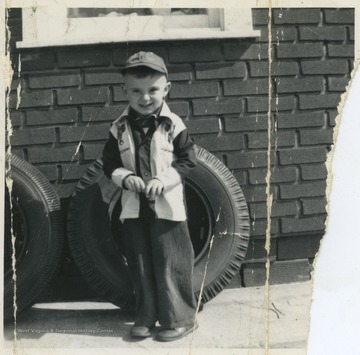 Butcher stands in front of a tire at Hitt's Filling Station in Weston, W. Va. He is 3 years old in this photograph. 