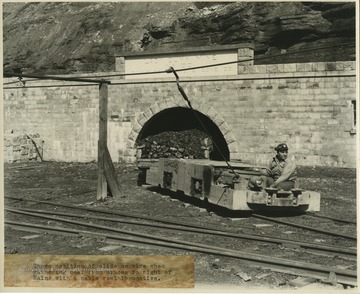 An unidentified coal miner leads the coal cart across the rails. 