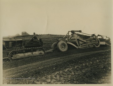 A man leads a large piece of equipment across a field. 