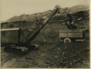 A miner uses a power shovel machine to load coal into a truck. 