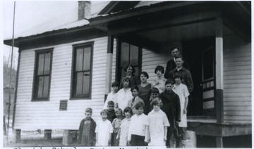 A group of school children pose outside of the school building with their teachers. Subjects unidentified. 