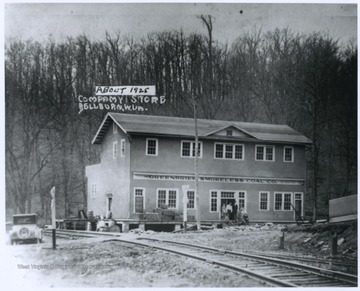 People are pictured at the store entrance. The building is situated beside railroad tracks. 