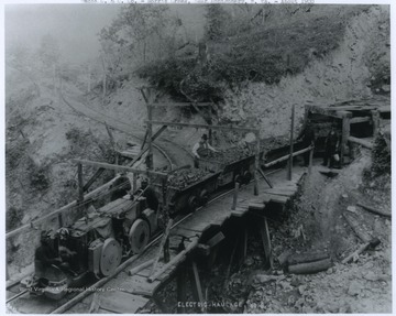 An electric haulage rail system at mine no. 2. An Africa-American miner is pictured in the conductor's seat on the train engine. Miners inspect the coal loaded into the carts before it is transported. 