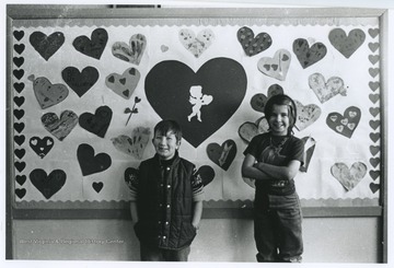 A young boy and girl stand beside their Valentine's Day art. 