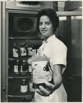 An unidentified female nurse holds a blood pack up to the camera. 