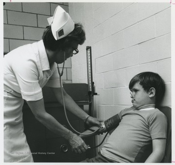 A nurse holds a stethoscope on a young boy's pulse. 