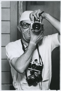 An unidentified man in scrubs holds up a camera to his face. 