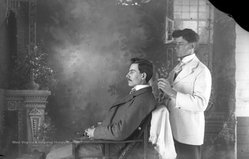 A man sits while a barber combs and styles his hair.