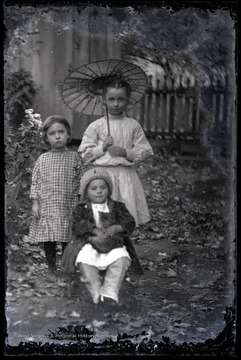 Three young girls are pictured, one holding a parasol and one holding a kitten. 