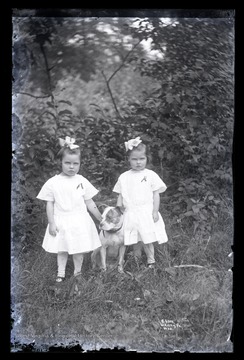 Two girl twins in identical outfits pose with their pet dog.